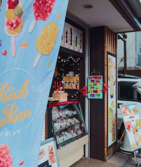 Colorful popsicle-themed shop banner beside a display case and menu boards at an ice cream store entrance.